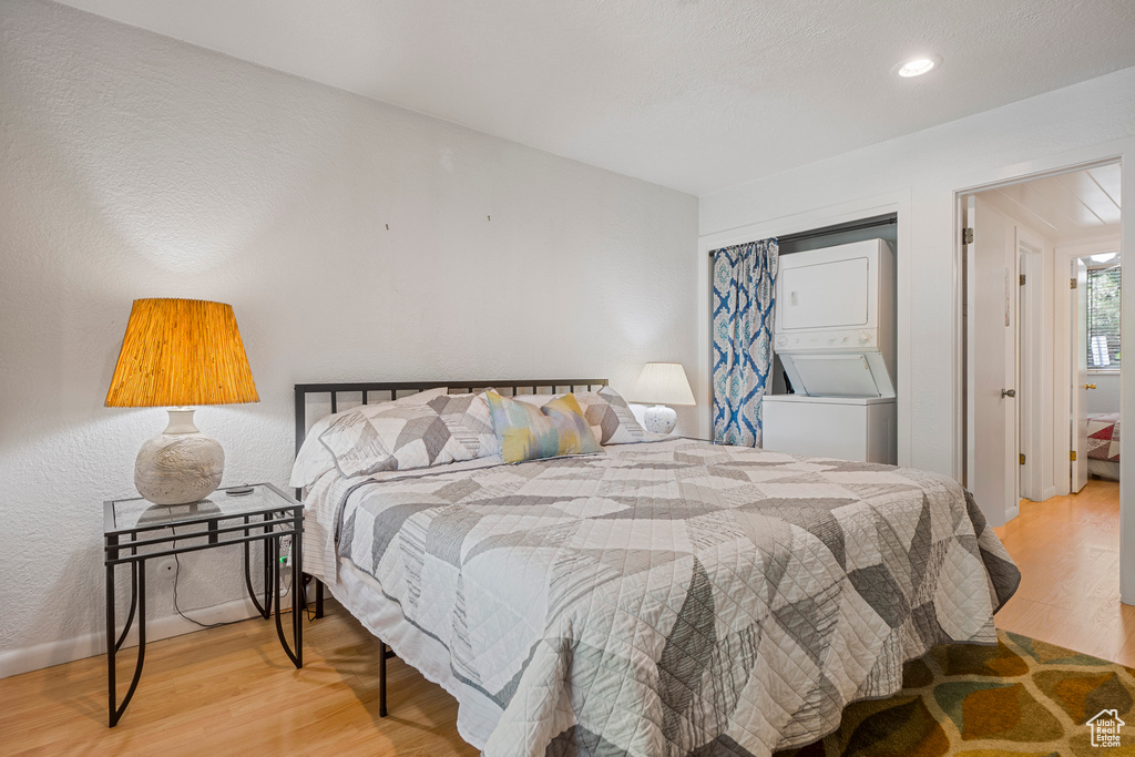 Bedroom with estacked washer and dryer, wood finished floors, a closet, recessed lighting, and baseboards