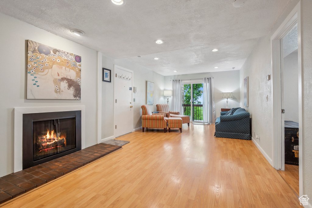 Living room featuring wood finished floors, a warm lit fireplace, recessed lighting, baseboards, and a textured ceiling