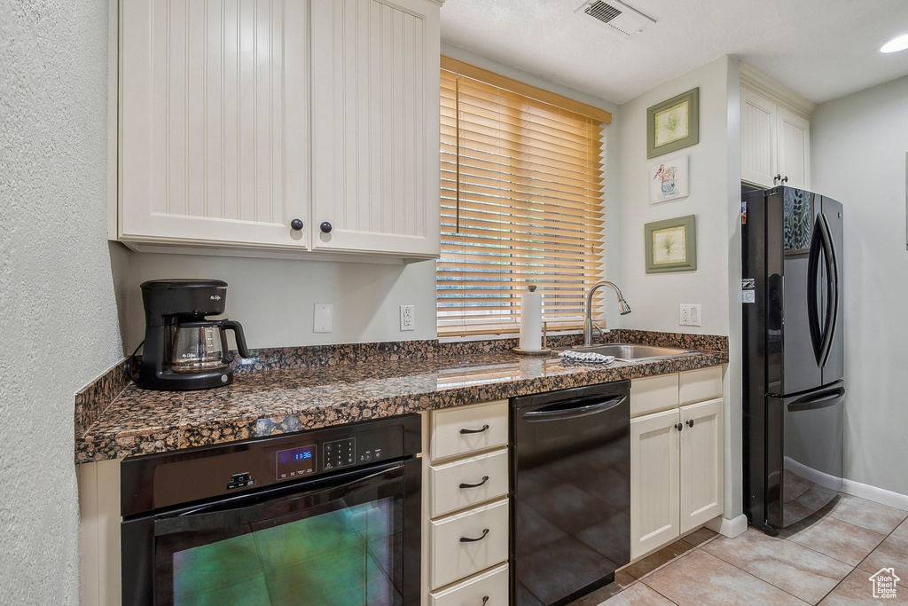 Kitchen featuring black appliances, dark countertops, a sink, light tile patterned floors, and white cabinetry