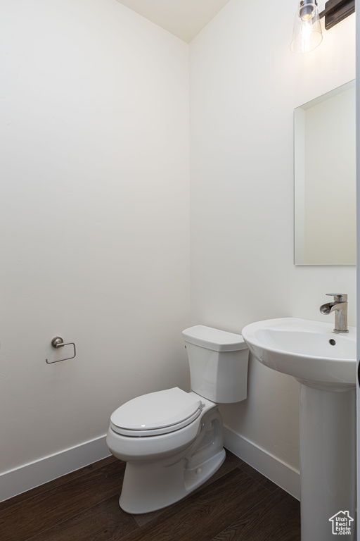 Half bath featuring baseboards, toilet, wood finished floors, and a sink