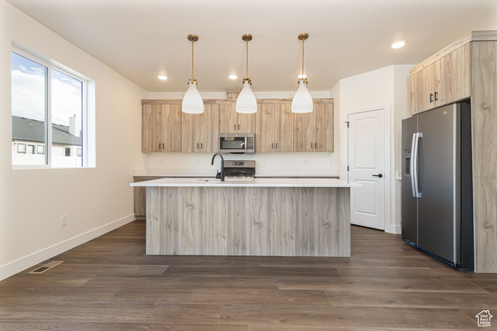 Kitchen featuring appliances with stainless steel finishes, light brown cabinetry, light countertops, an island with sink, and recessed lighting