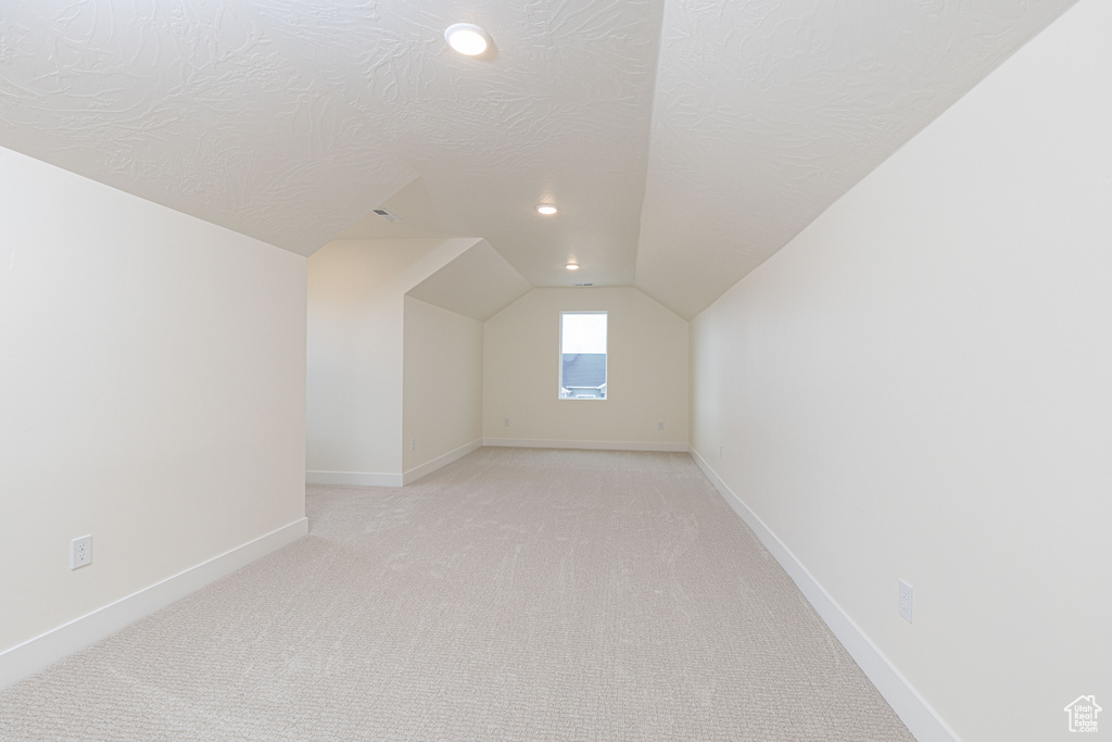 Additional living space with vaulted ceiling, light colored carpet, baseboards, a textured ceiling, and recessed lighting