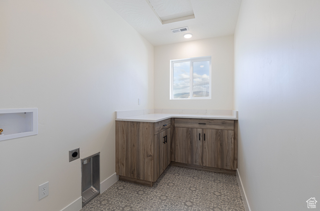 Laundry room with electric dryer hookup, baseboards, cabinet space, and light flooring