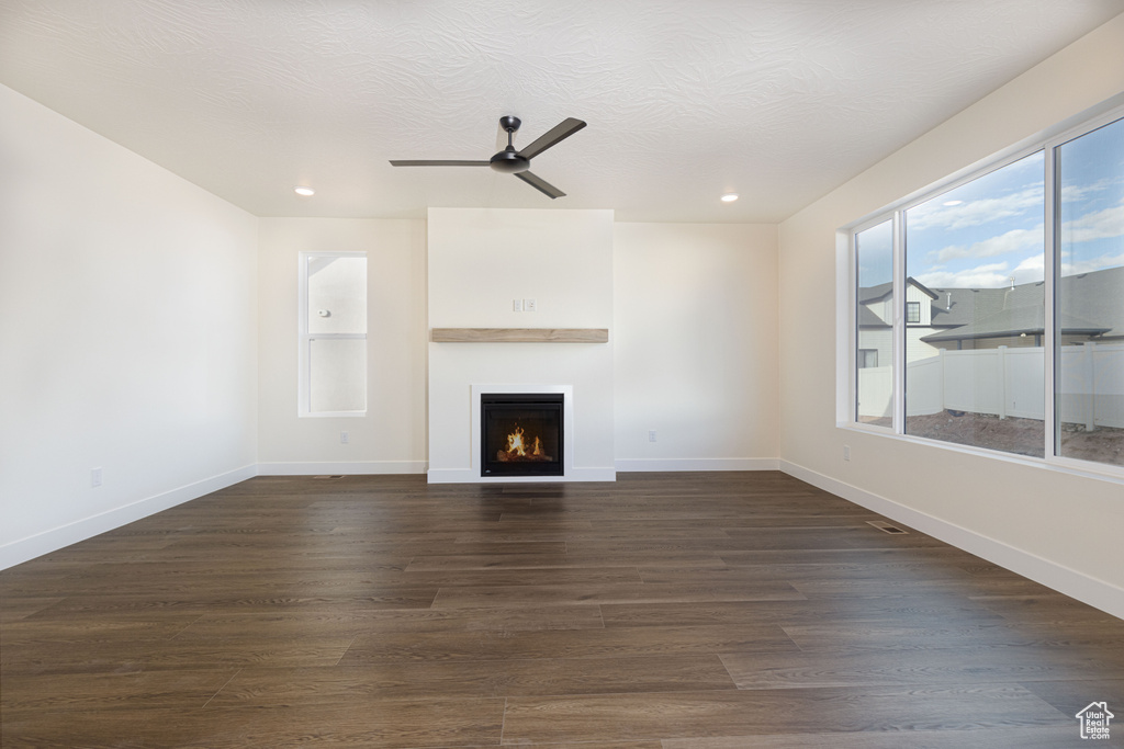 Unfurnished living room featuring a lit fireplace, ceiling fan, dark wood-style floors, recessed lighting, and baseboards