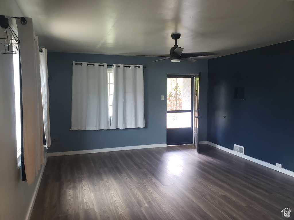 Empty room with dark wood finished floors, a ceiling fan, and baseboards