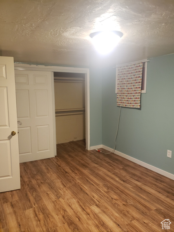 Unfurnished bedroom featuring wood finished floors, a closet, baseboards, and a textured ceiling