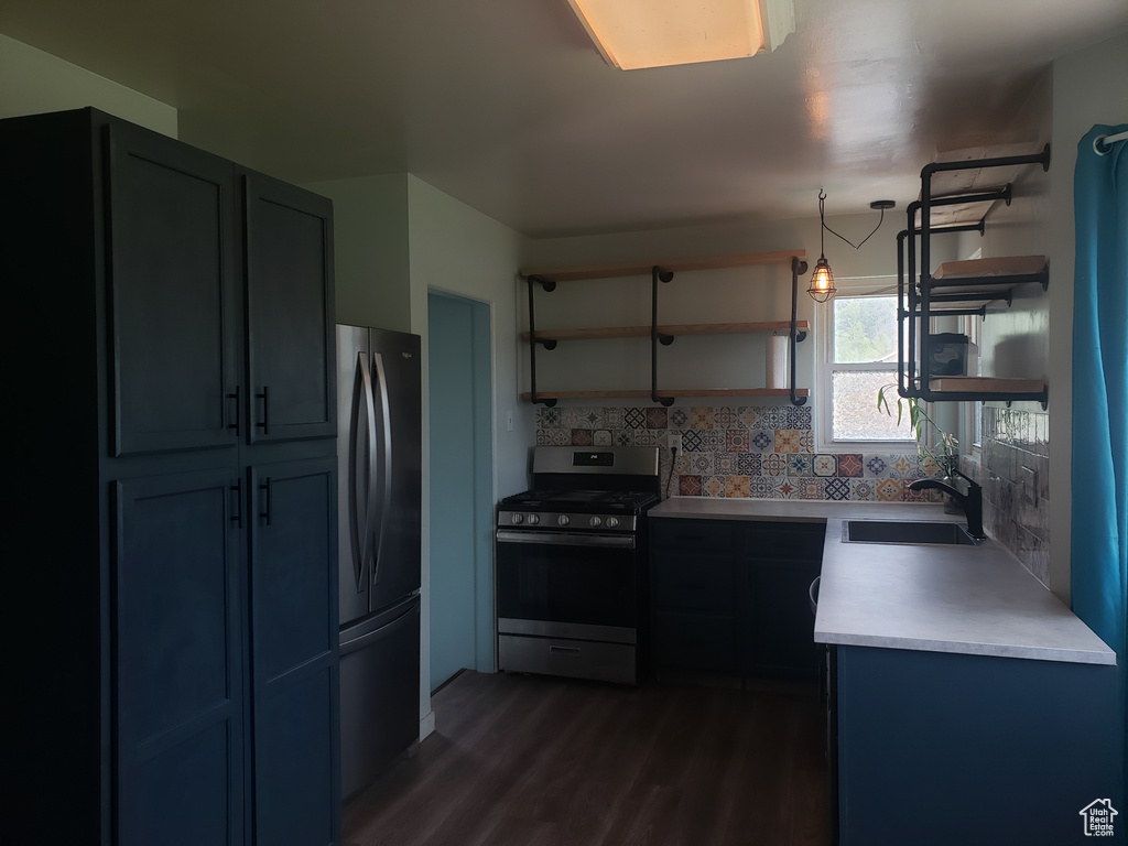 Kitchen with appliances with stainless steel finishes, open shelves, a sink, dark wood finished floors, and tasteful backsplash