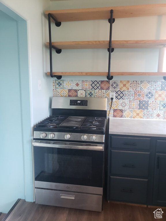 Kitchen with stainless steel gas range oven, open shelves, tasteful backsplash, dark wood-style floors, and light countertops