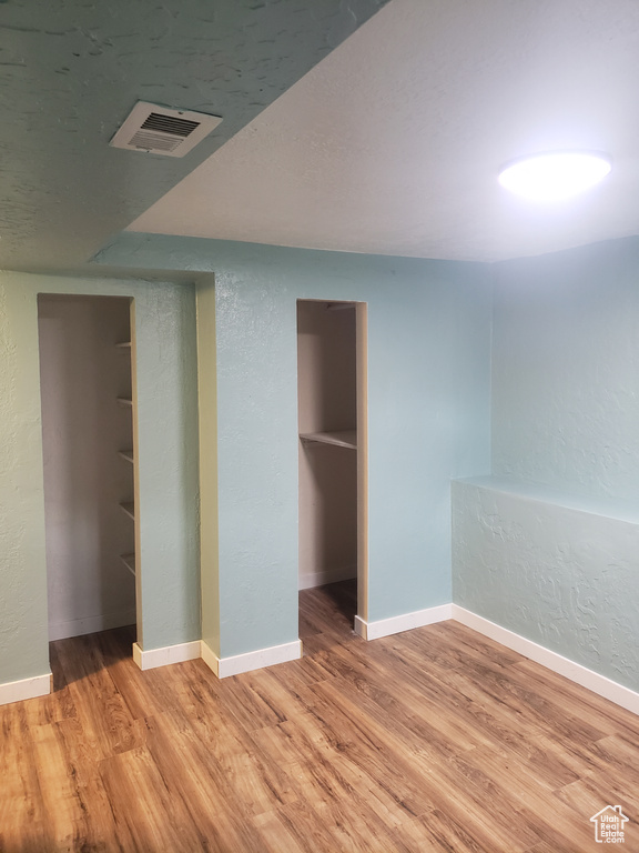 Unfurnished bedroom with light wood-style flooring, a textured wall, and baseboards