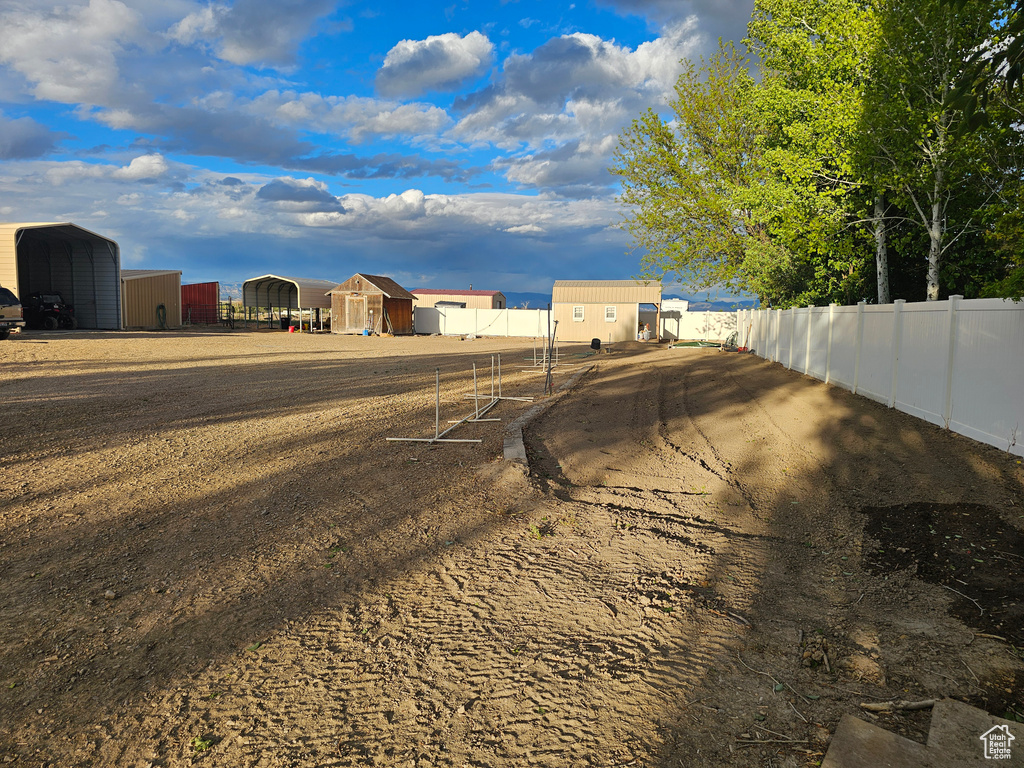 View of yard with fence, a carport, and an outbuilding