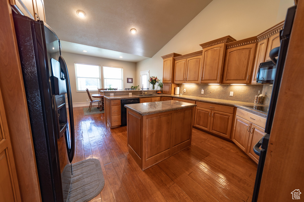 Kitchen with black appliances, a peninsula, dark wood-type flooring, a sink, and lofted ceiling