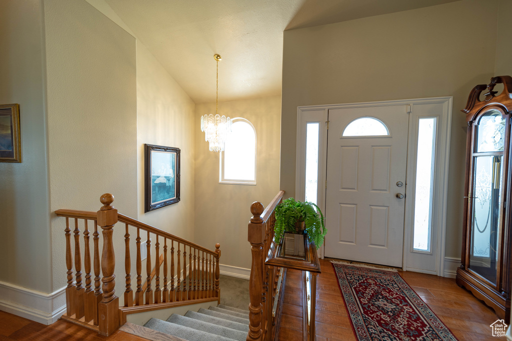 Entrance foyer featuring a chandelier, lofted ceiling, wood finished floors, baseboards, and stairway