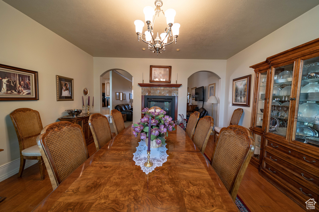 Dining area with arched walkways, wood finished floors, a chandelier, and a tiled fireplace