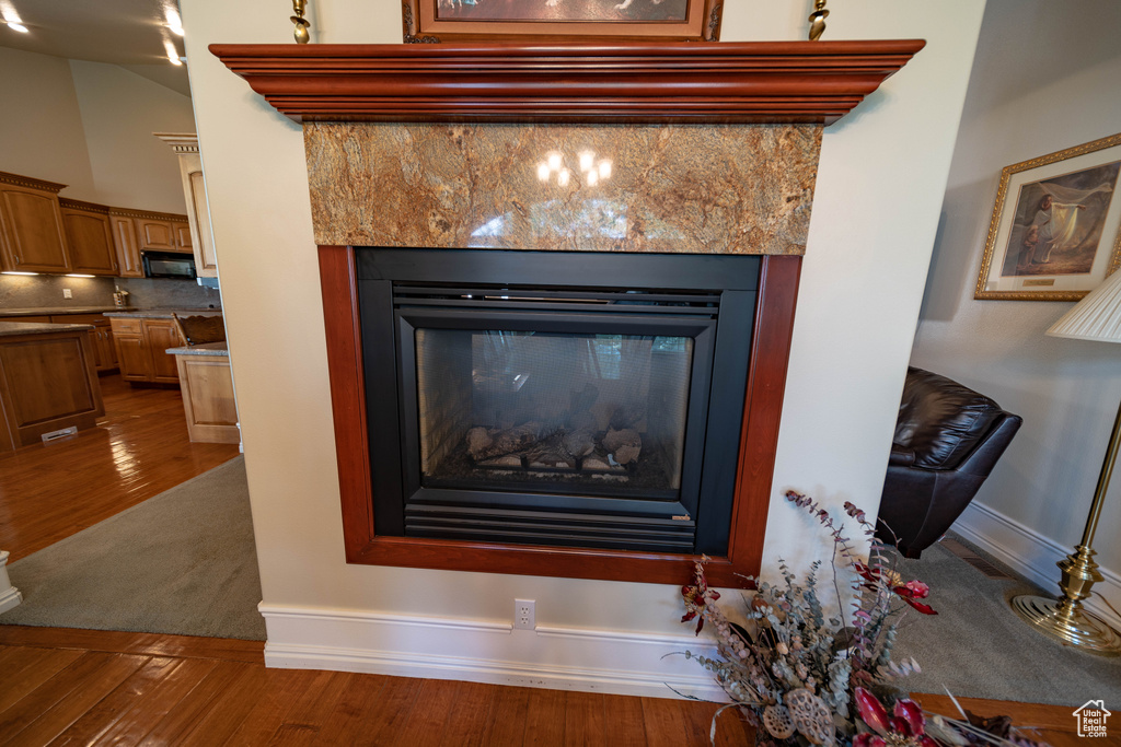 Detailed view of a glass covered fireplace, wood finished floors, black microwave, baseboards, and backsplash