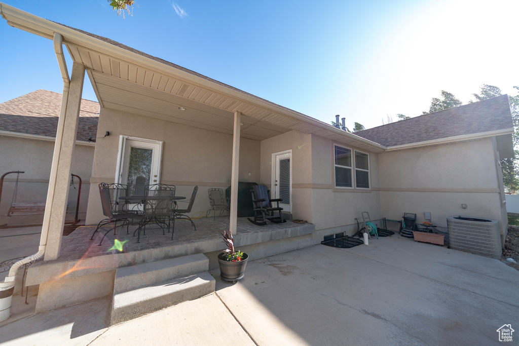 Back of house with a patio area, stucco siding, central AC unit, and a shingled roof