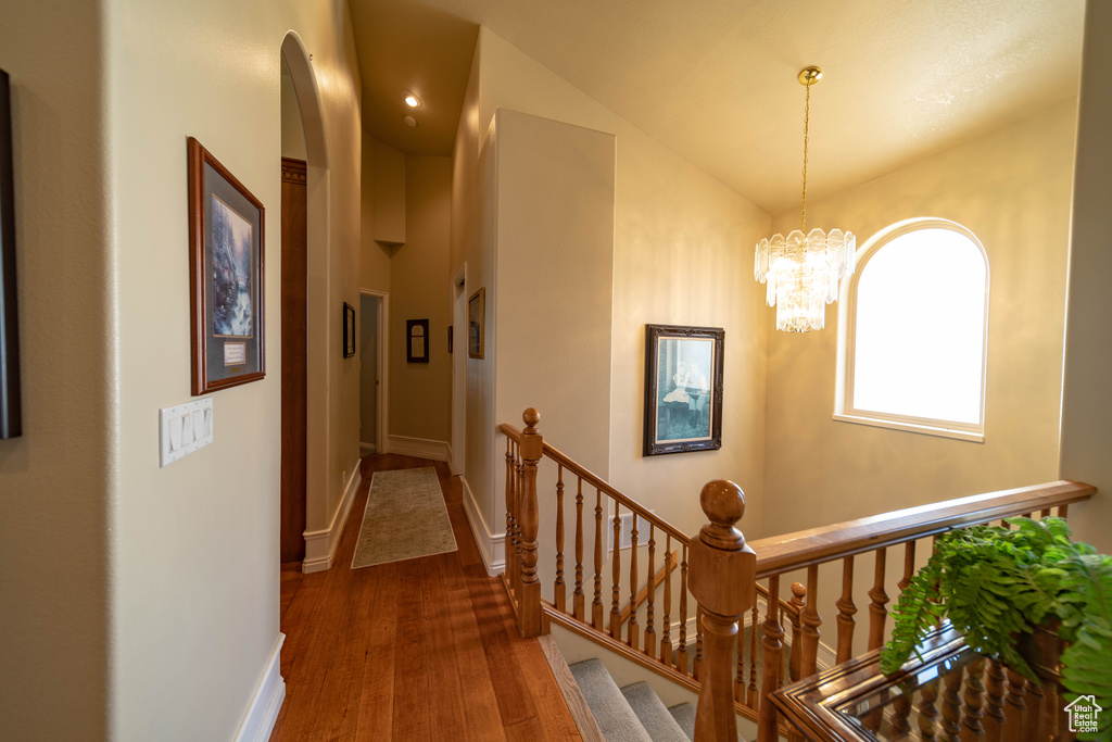 Hallway featuring wood finished floors, vaulted ceiling, arched walkways, a chandelier, and baseboards