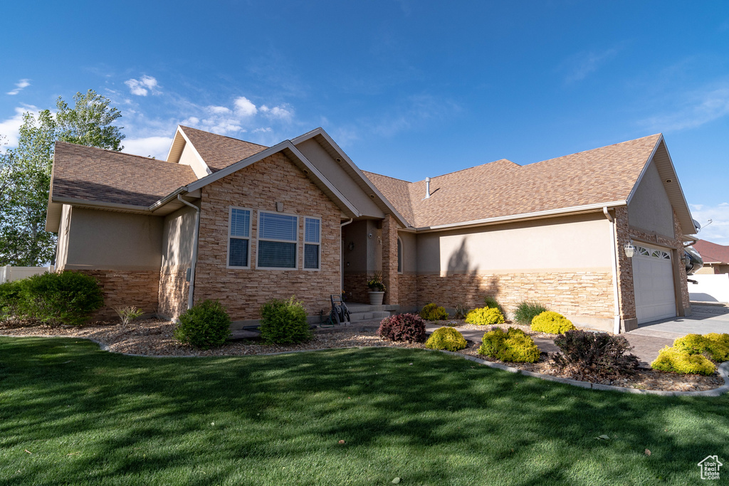 Ranch-style home with stone siding, stucco siding, a front lawn, and an attached garage