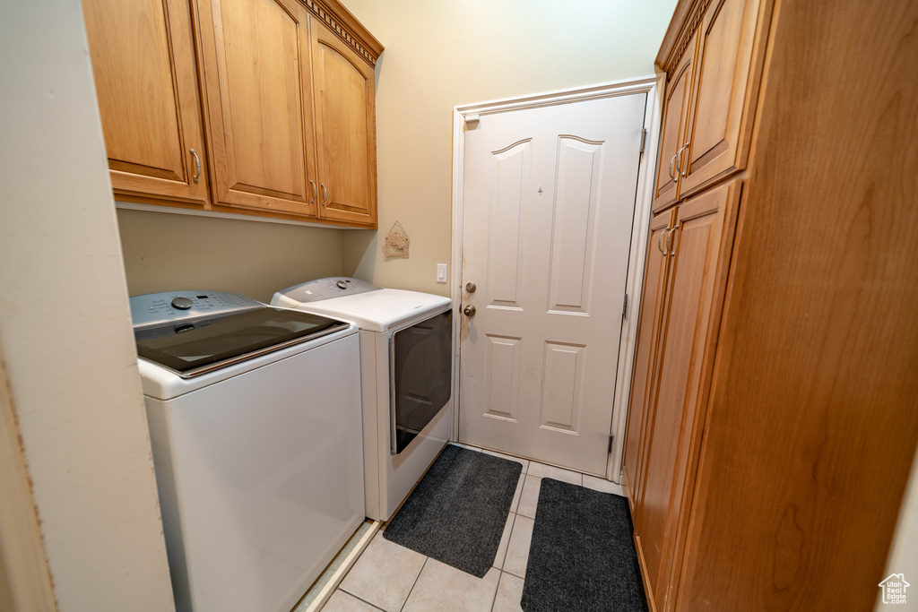 Laundry area with washing machine and clothes dryer, cabinet space, and light tile patterned flooring