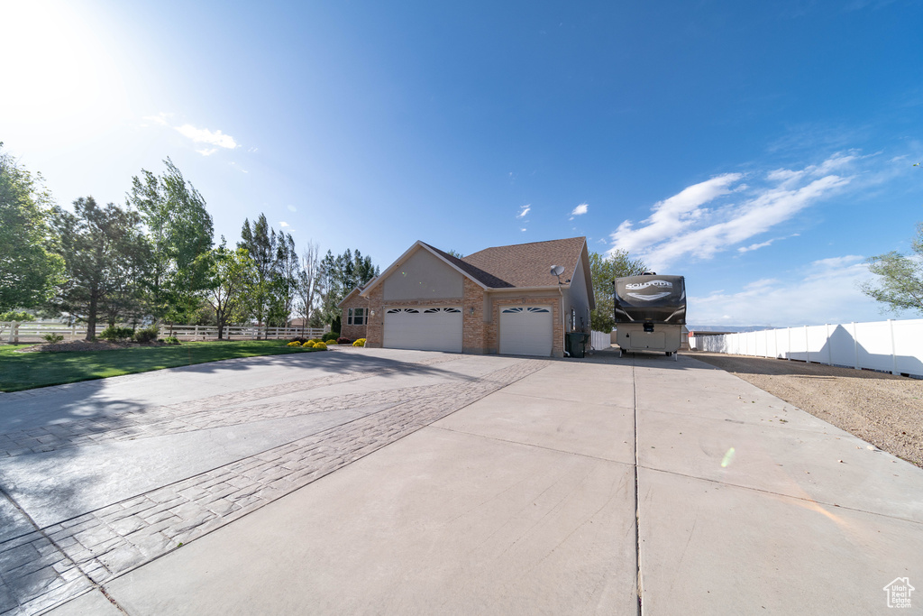 View of front of property featuring driveway, an attached garage, brick siding, and fence