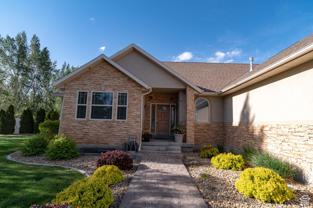 View of exterior entry featuring stone siding, stucco siding, and roof with shingles