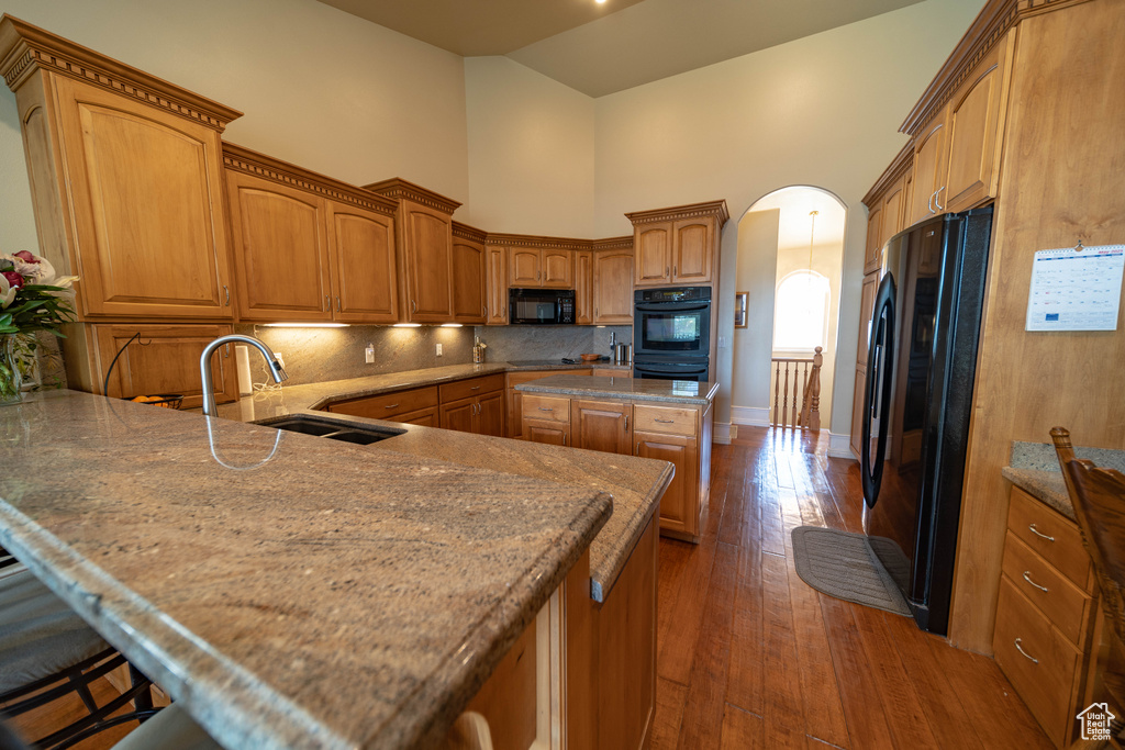 Kitchen featuring black appliances, arched walkways, a sink, dark wood-style floors, and decorative backsplash
