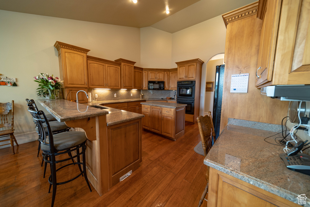 Kitchen with black appliances, arched walkways, backsplash, dark wood-type flooring, and a peninsula