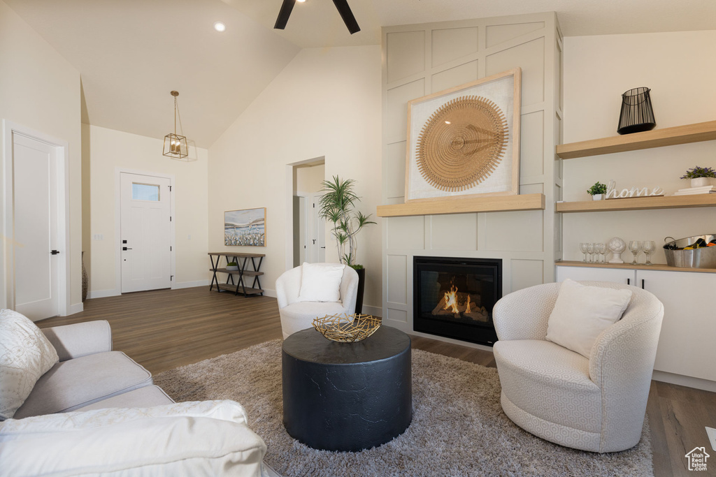 Living room featuring a ceiling fan, wood finished floors, a glass covered fireplace, baseboards, and high vaulted ceiling