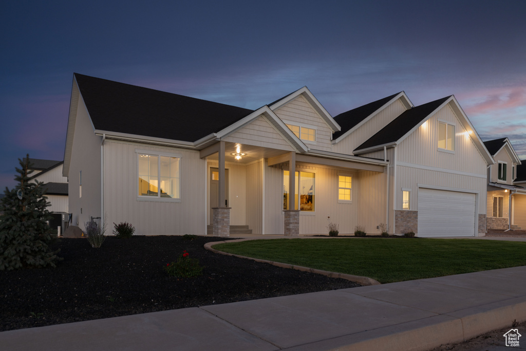 View of front of house with an attached garage, a lawn, covered porch, and stone siding