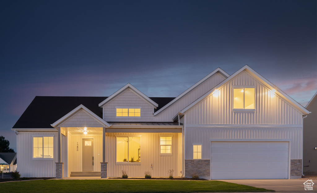 Modern farmhouse with a front yard, a standing seam roof, driveway, board and batten siding, and an attached garage