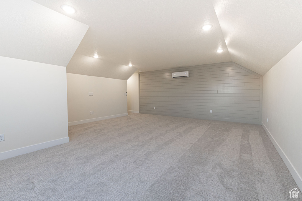Bonus room featuring vaulted ceiling, a wall unit AC, light colored carpet, baseboards, and recessed lighting