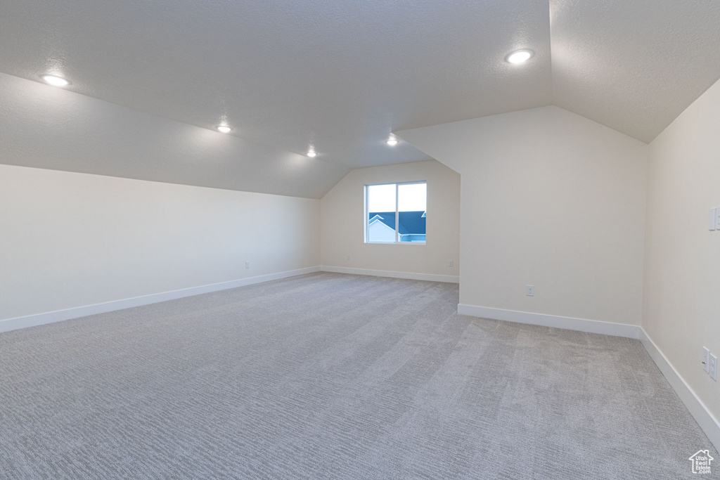 Additional living space with vaulted ceiling, light colored carpet, and baseboards