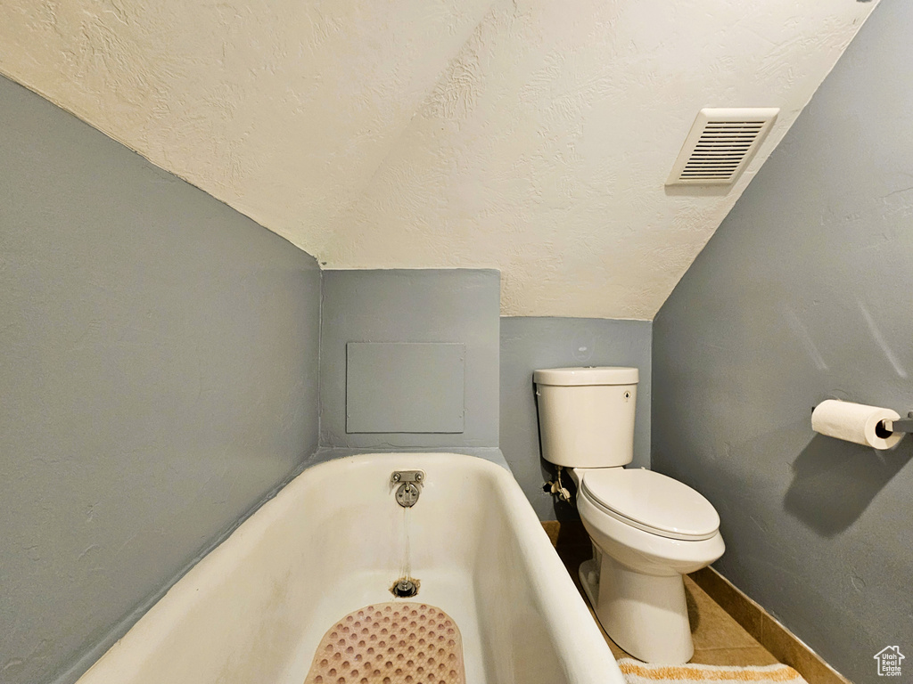 Bathroom with a tub, a textured ceiling, toilet, lofted ceiling, and baseboards