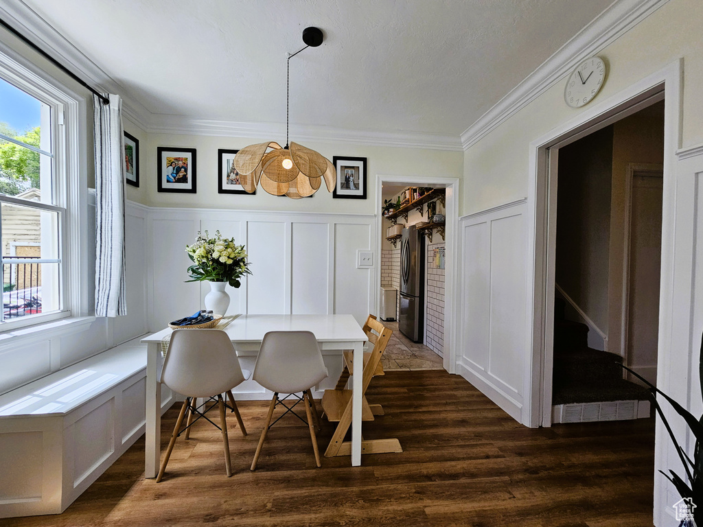 Dining room featuring a decorative wall, plenty of natural light, crown molding, dark wood-style floors, and wainscoting