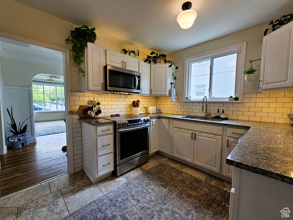 Kitchen featuring stainless steel appliances, a sink, backsplash, white cabinetry, and crown molding