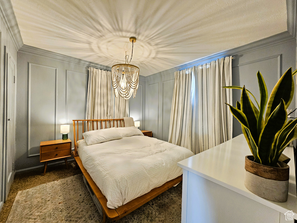 Bedroom featuring a decorative wall, dark colored carpet, a chandelier, and crown molding