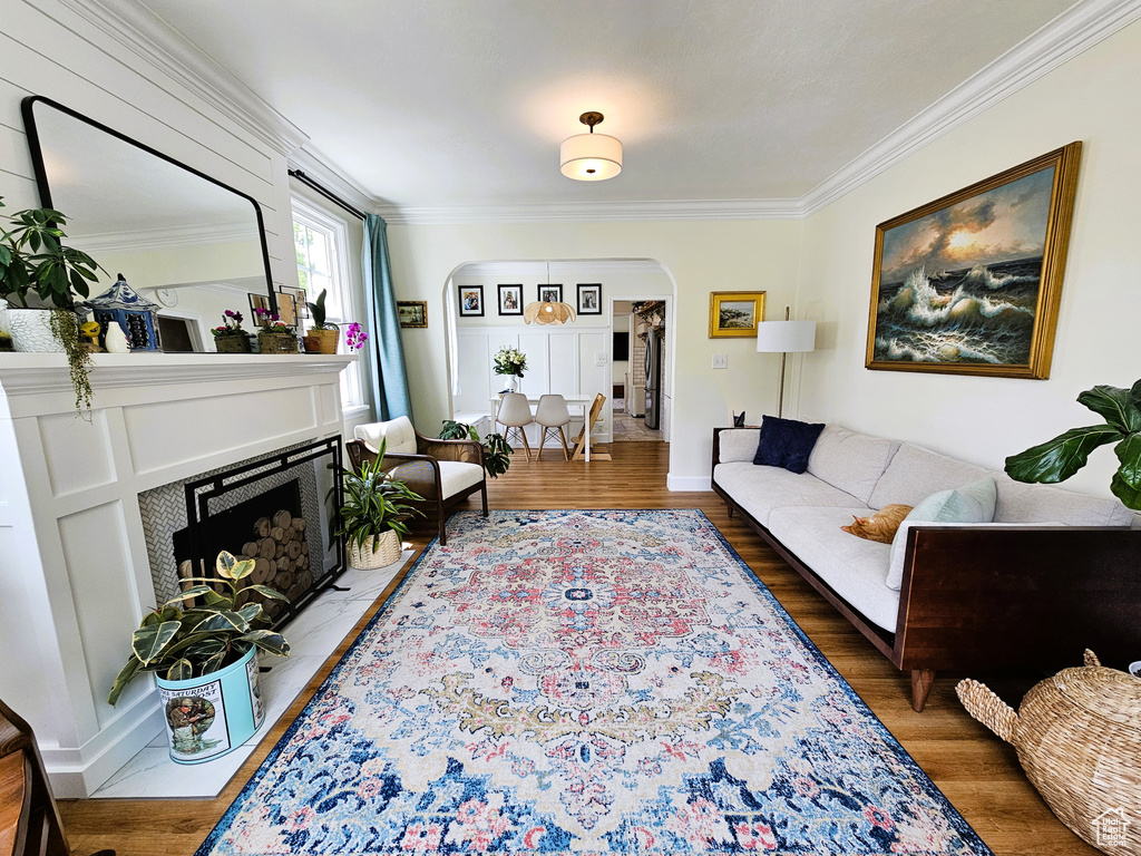 Living area with arched walkways, ornamental molding, wood finished floors, and a fireplace with flush hearth