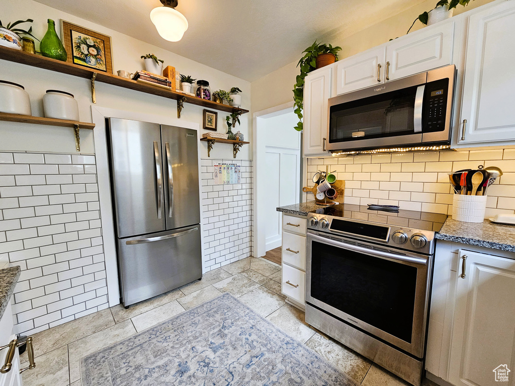 Kitchen featuring appliances with stainless steel finishes, open shelves, tile walls, white cabinetry, and dark stone counters