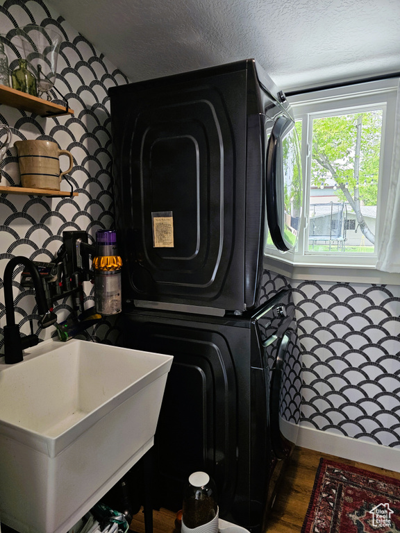 Laundry room featuring a textured ceiling, estacked washer and dryer, and wood finished floors