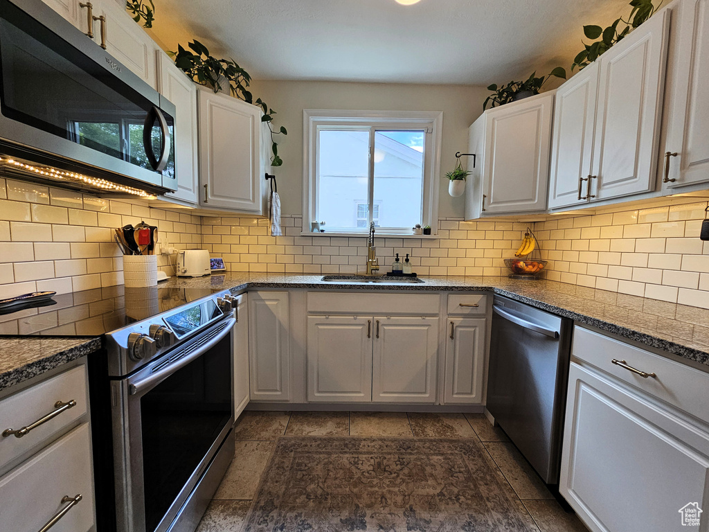 Kitchen featuring stainless steel appliances, a sink, white cabinetry, decorative backsplash, and dark stone counters