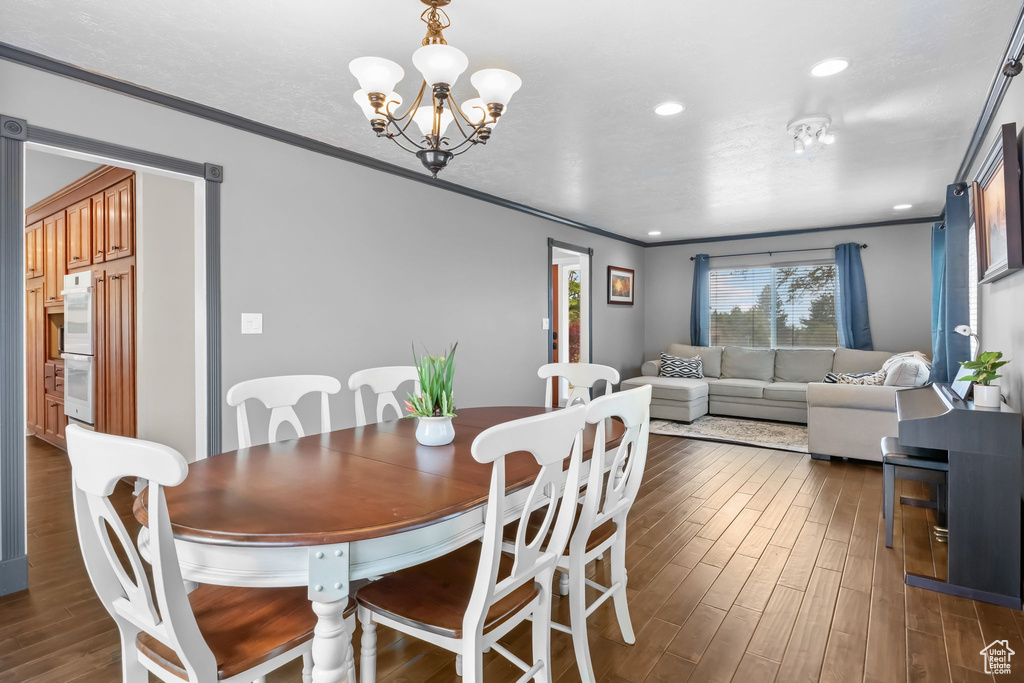 Dining room with crown molding, dark wood finished floors, a chandelier, and recessed lighting
