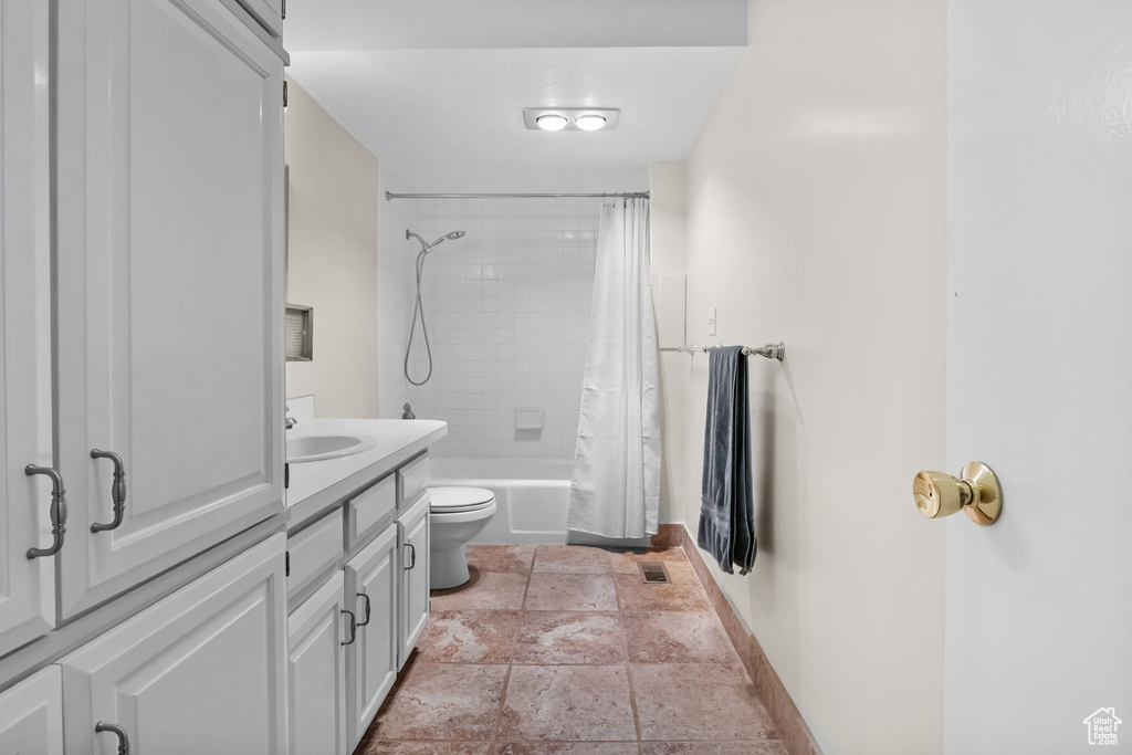 Bathroom with baseboards, stone tile flooring, toilet, shower / bath combo, and vanity