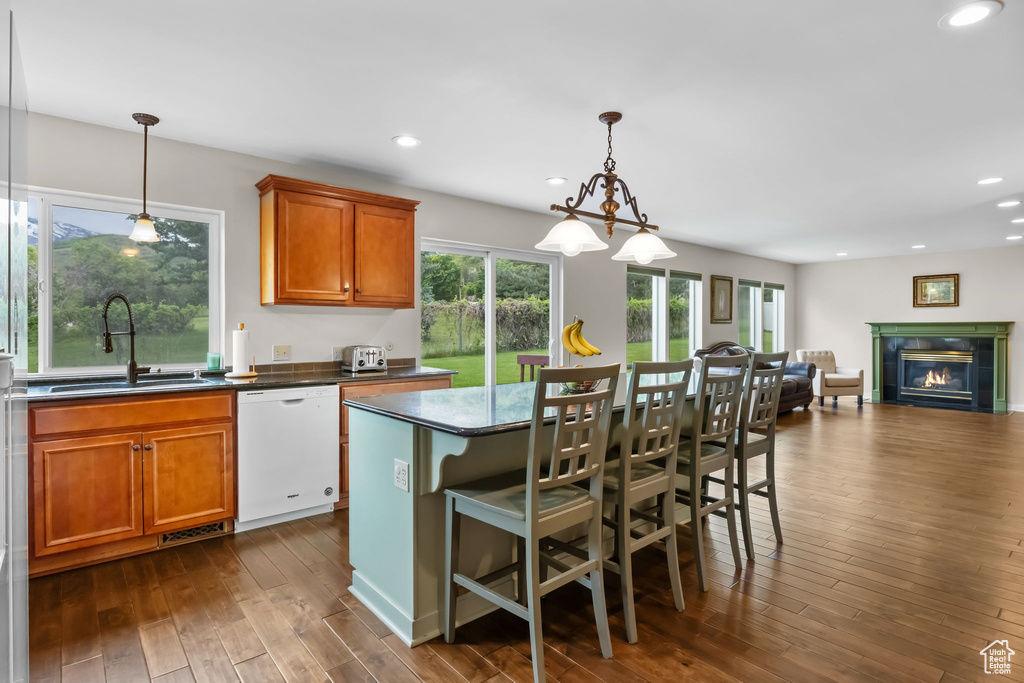 Kitchen with dishwasher, a sink, dark wood-style flooring, a tiled fireplace, and brown cabinetry