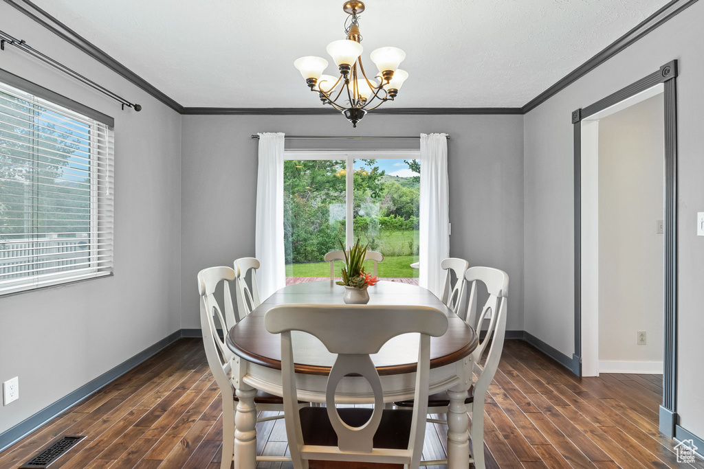 Dining area with dark wood-style floors, baseboards, crown molding, and a chandelier