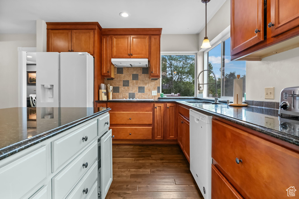 Kitchen featuring white appliances, under cabinet range hood, brown cabinets, dark wood-style floors, and recessed lighting