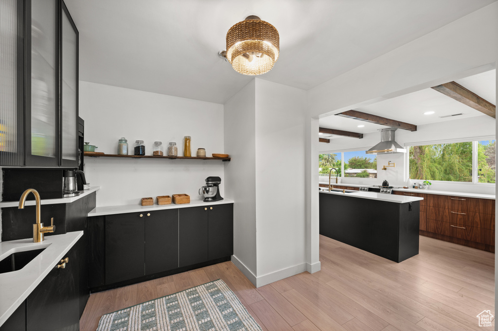Bar with wall chimney range hood, a sink, light wood-style flooring, beam ceiling, and baseboards