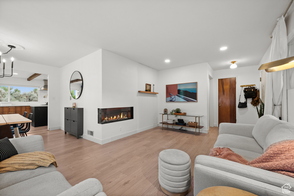 Living room with light wood-type flooring, a chandelier, a glass covered fireplace, recessed lighting, and baseboards