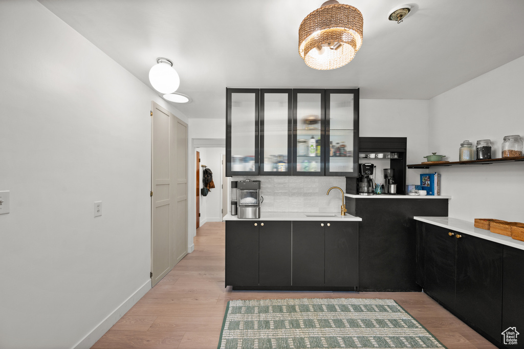 Kitchen featuring dark cabinetry, light countertops, light wood-type flooring, and backsplash