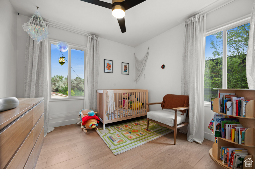 Bedroom with a nursery area, multiple windows, and light wood-style flooring