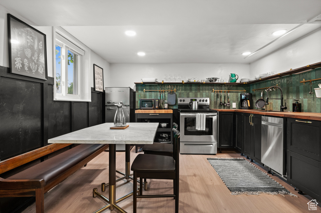 Kitchen with stainless steel appliances, wood counters, dark cabinets, open shelves, and light wood-style floors