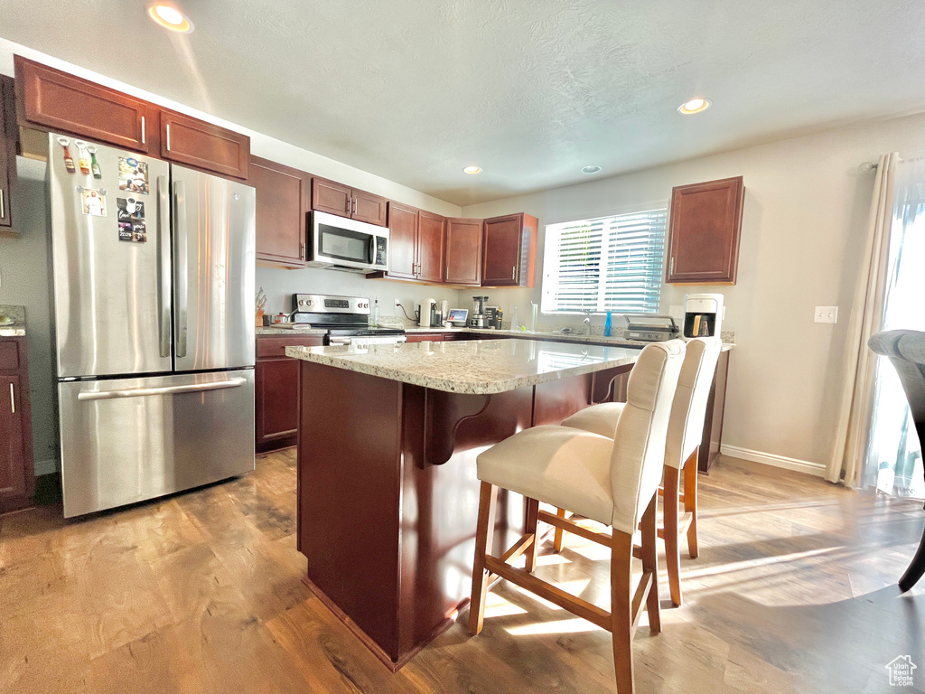 Kitchen with appliances with stainless steel finishes, a center island, light wood-type flooring, a kitchen bar, and plenty of natural light